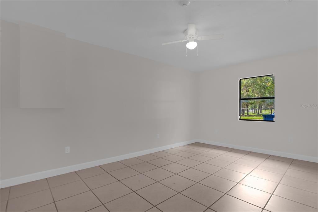 An empty room with light-colored tile flooring, white walls, a ceiling fan, and one window — 1349 E WISCONSIN AVENUE, DELAND, FL