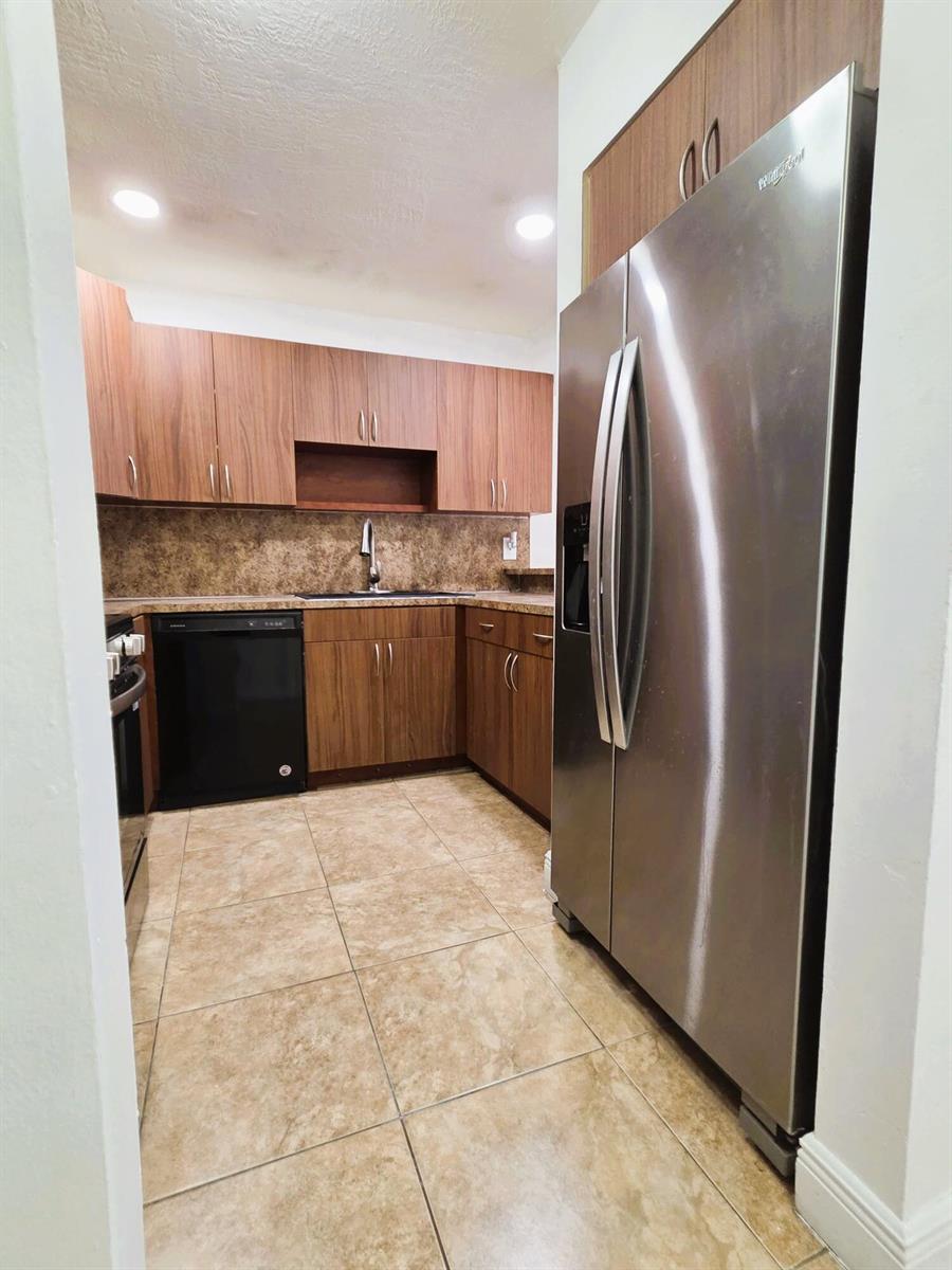 A kitchen features wood-grain cabinets, stainless steel appliances, a black dishwasher, and tiled flooring — 7000 NW 186th Street # 316, Hialeah FL 33015, HIALEAH, FL