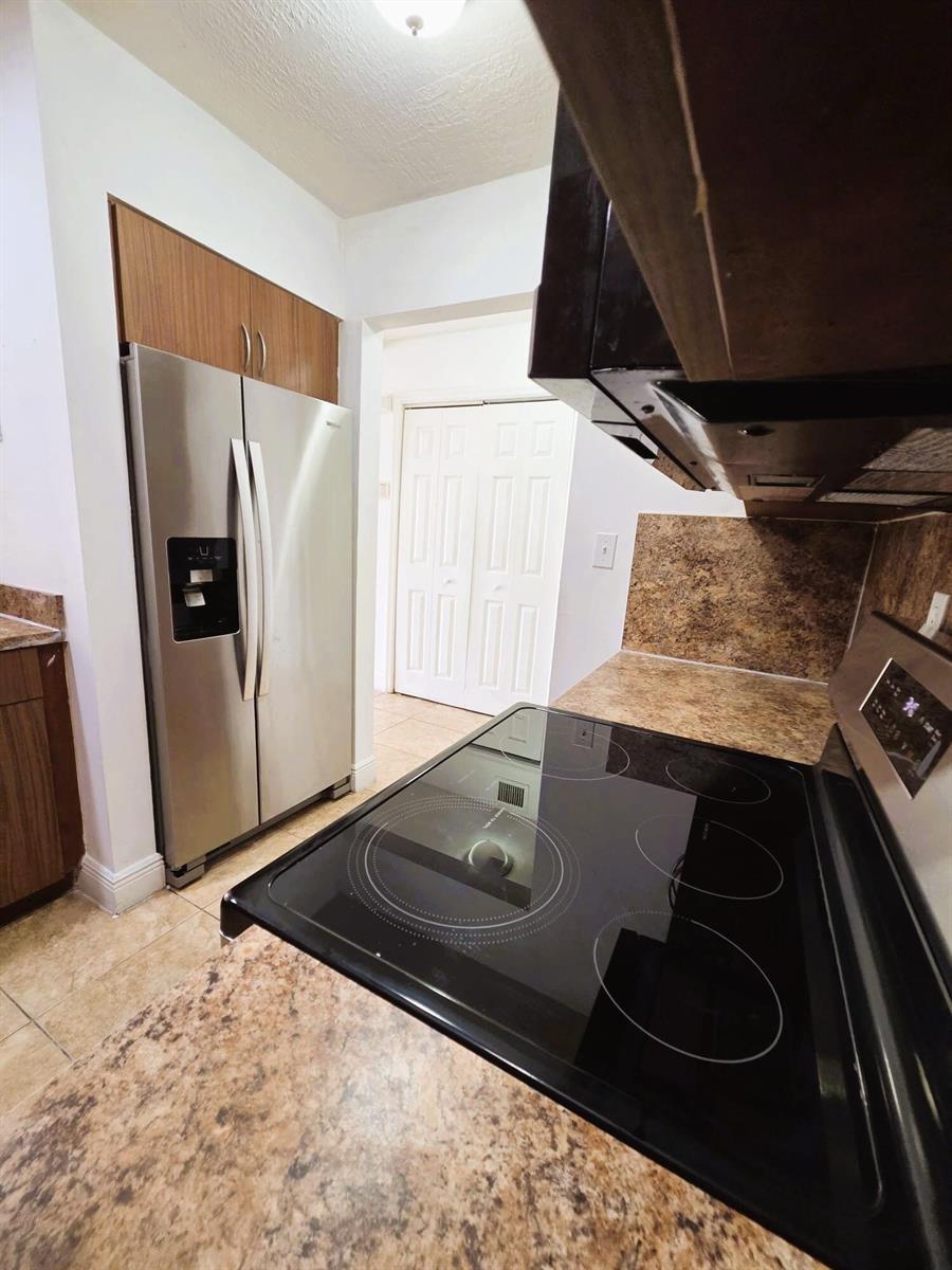 A kitchen features a stainless steel refrigerator, a black electric stove, and brown countertops — 7000 NW 186th Street # 316, Hialeah FL 33015, HIALEAH, FL