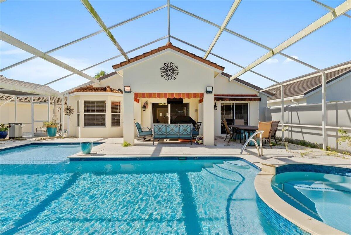 A backyard swimming pool and hot tub sit beneath a screened-in lanai behind a house — 7534 Ironbridge Circle, Delray Beach FL 33446, DELRAY BEACH, FL