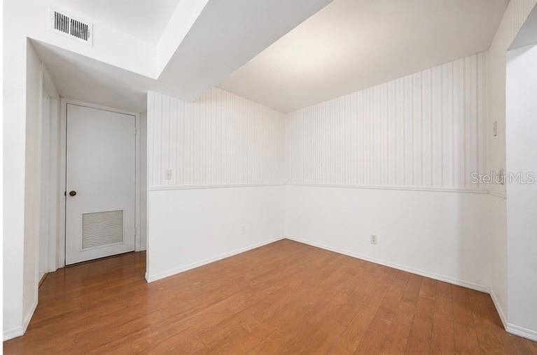 An empty room features wood-look flooring, white wainscoting, and vertical striped wallpaper — 10200 GANDY BOULEVARD N UNIT 714, ST PETERSBURG, FL