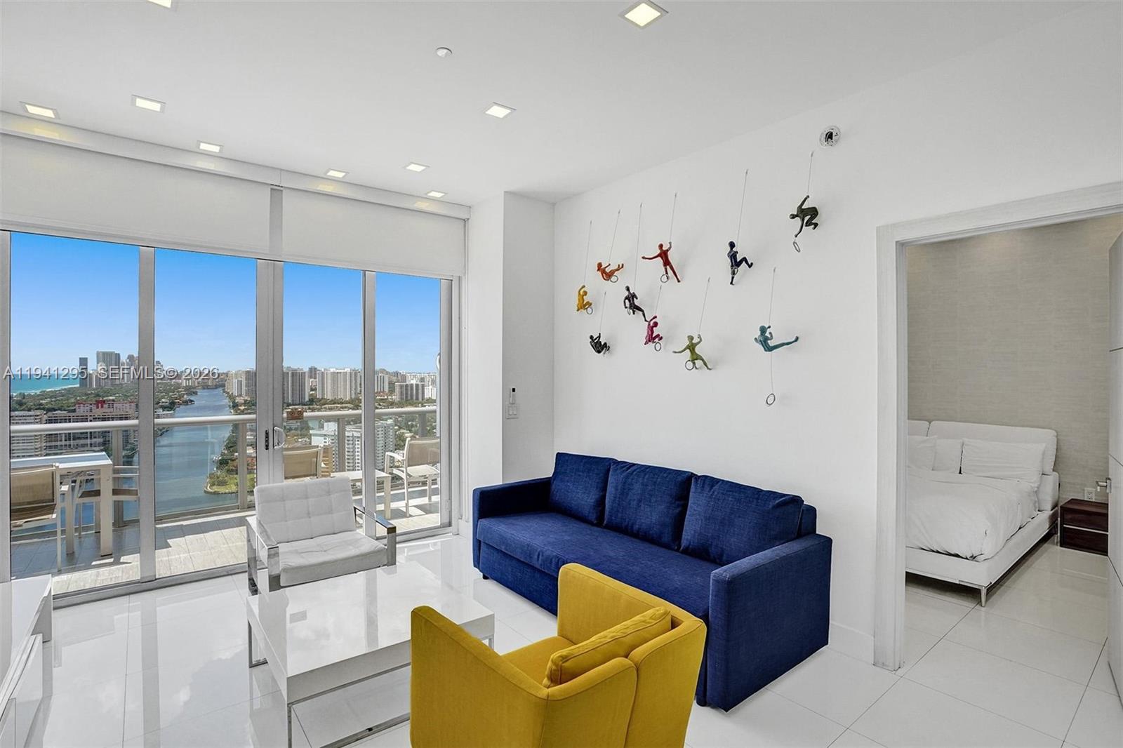 A modern living room features a blue sofa, yellow armchair, and wall-mounted climber figurines — 2600 E Hallandale Beach Blvd # T3303, Hallandale Beach FL 33009, HALLANDALE BEACH, FL