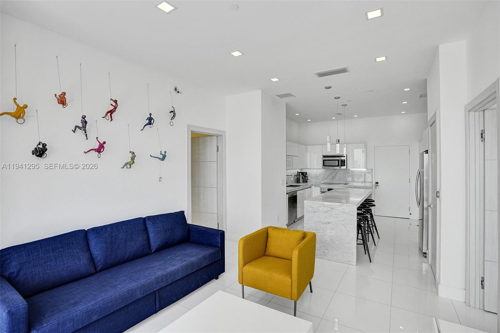 A modern open-concept living area features a blue sofa, yellow armchair, and white kitchen — 2600 E Hallandale Beach Blvd # T3303, Hallandale Beach FL 33009, HALLANDALE BEACH, FL