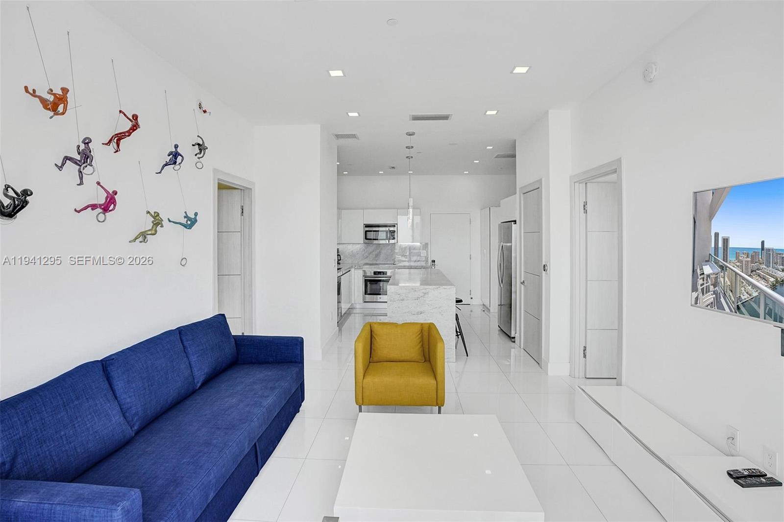 A modern living room features a blue sofa, yellow armchair, and wall-mounted climbing figure decor — 2600 E Hallandale Beach Blvd # T3303, Hallandale Beach FL 33009, HALLANDALE BEACH, FL