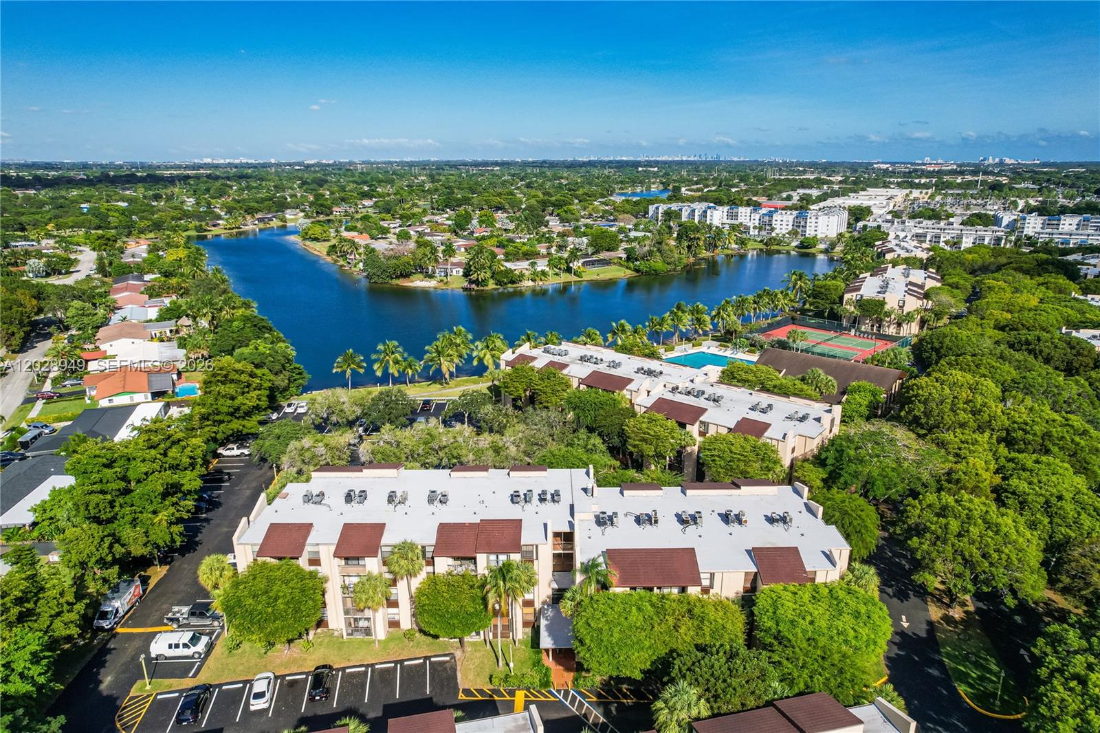 An aerial view shows multi-story apartment buildings, a lake, tennis courts, and surrounding lush greenery — 14501 N Kendall Dr # 212H, Miami FL 33186, MIAMI, FL