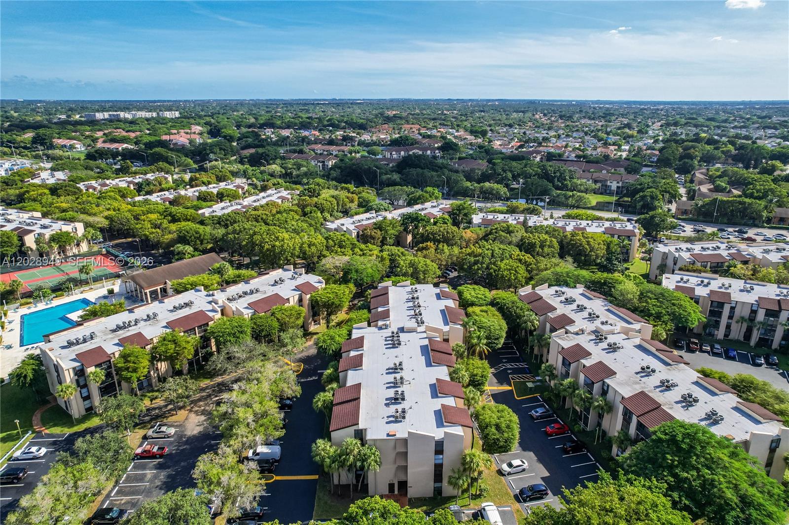 An aerial view shows multiple multi-story apartment buildings surrounded by trees, parking lots, and a pool — 14501 N Kendall Dr # 212H, Miami FL 33186, MIAMI, FL