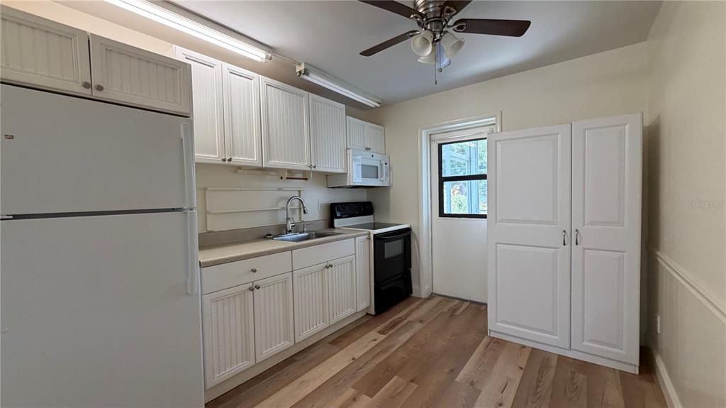 A kitchen features white cabinetry, a black stove, a refrigerator, and light wood flooring — 10147 TRAMORE AVENUE UNIT #A, ENGLEWOOD, FL