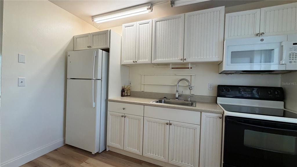 A kitchen features white cabinets, a white refrigerator, a stainless steel sink, and a stove — 10147 TRAMORE AVENUE UNIT #A, ENGLEWOOD, FL
