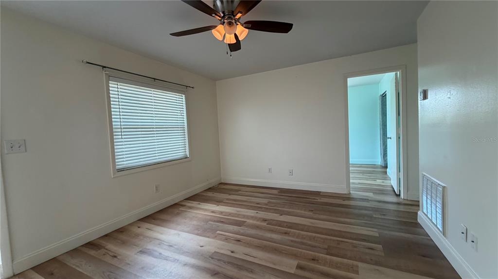 An empty bedroom features light-colored wood-look flooring, white walls, a ceiling fan, and a window — 10147 TRAMORE AVENUE UNIT #A, ENGLEWOOD, FL
