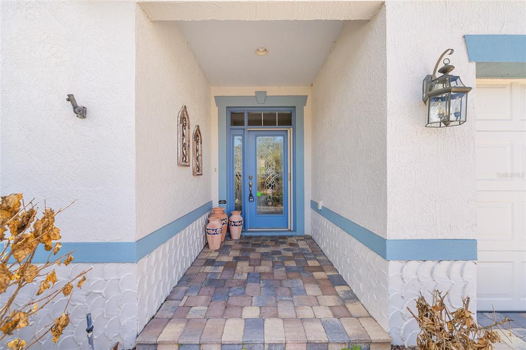A covered entryway features a blue front door, stone-look pavers, and decorative wall accents — 646 STRATFORD LANE, THE VILLAGES, FL