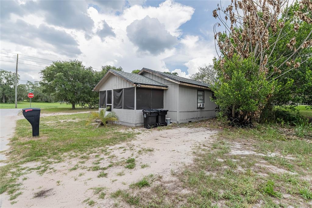 A small, grey, single-story house with a screened-in porch sits on a sandy lot — 5 NORTH STREET, FROSTPROOF, FL