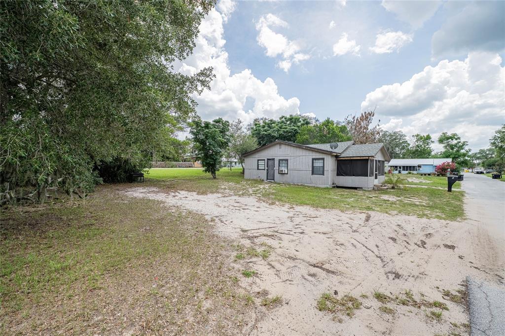 A single-story house with light-colored siding sits on a sandy lot next to a road — 5 NORTH STREET, FROSTPROOF, FL