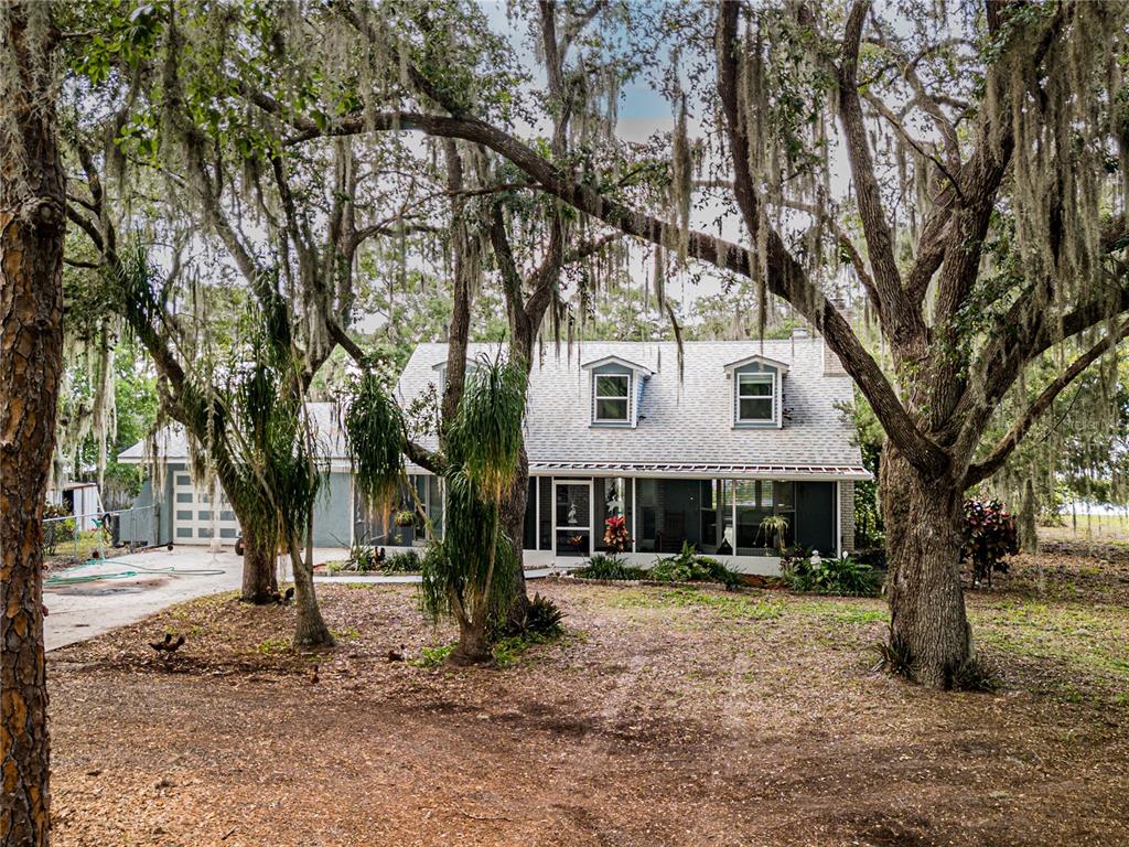 A two-story house with a screened porch and dormer windows sits among large, moss-covered trees — 1502 LAKE JOSEPHINE DRIVE, SEBRING, FL