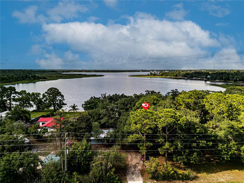 An aerial view shows a wooded lot with a red-roofed house near a lake — 1502 LAKE JOSEPHINE DRIVE, SEBRING, FL
