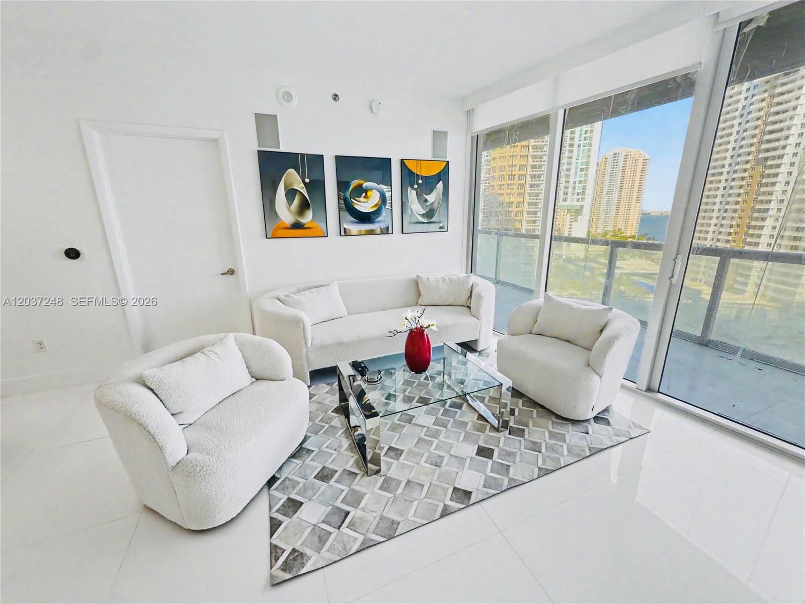 A modern living room features white furniture, a glass coffee table, and floor-to-ceiling windows — 465 Brickell Ave # 1605, Miami FL 33131, MIAMI, FL