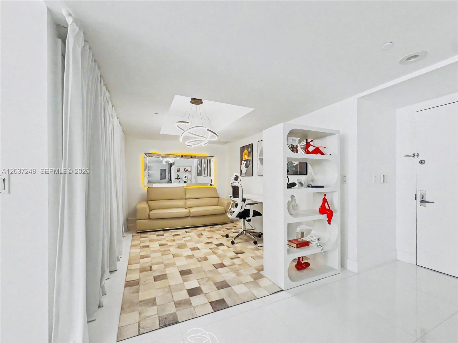 A modern room features a beige sofa, a desk, a white bookshelf, and a patterned rug — 465 Brickell Ave # 1605, Miami FL 33131, MIAMI, FL
