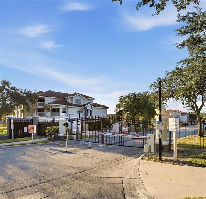 A gated entrance with a security arm and metal fencing leads to a multi-story apartment building — 13803 FAIRWAY ISLAND DRIVE UNIT 1618, ORLANDO, FL
