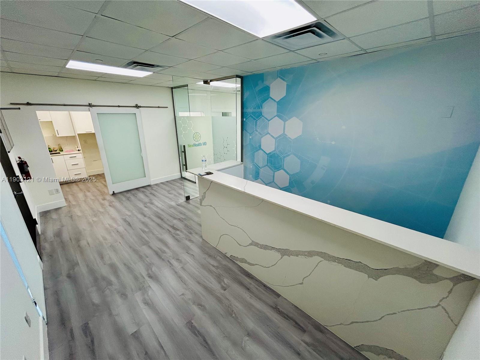 A reception area features a marble-topped desk, wood-look flooring, and a blue hexagonal wall mural — 10305 NW 41st St # 216, Doral FL 33178, DORAL, FL