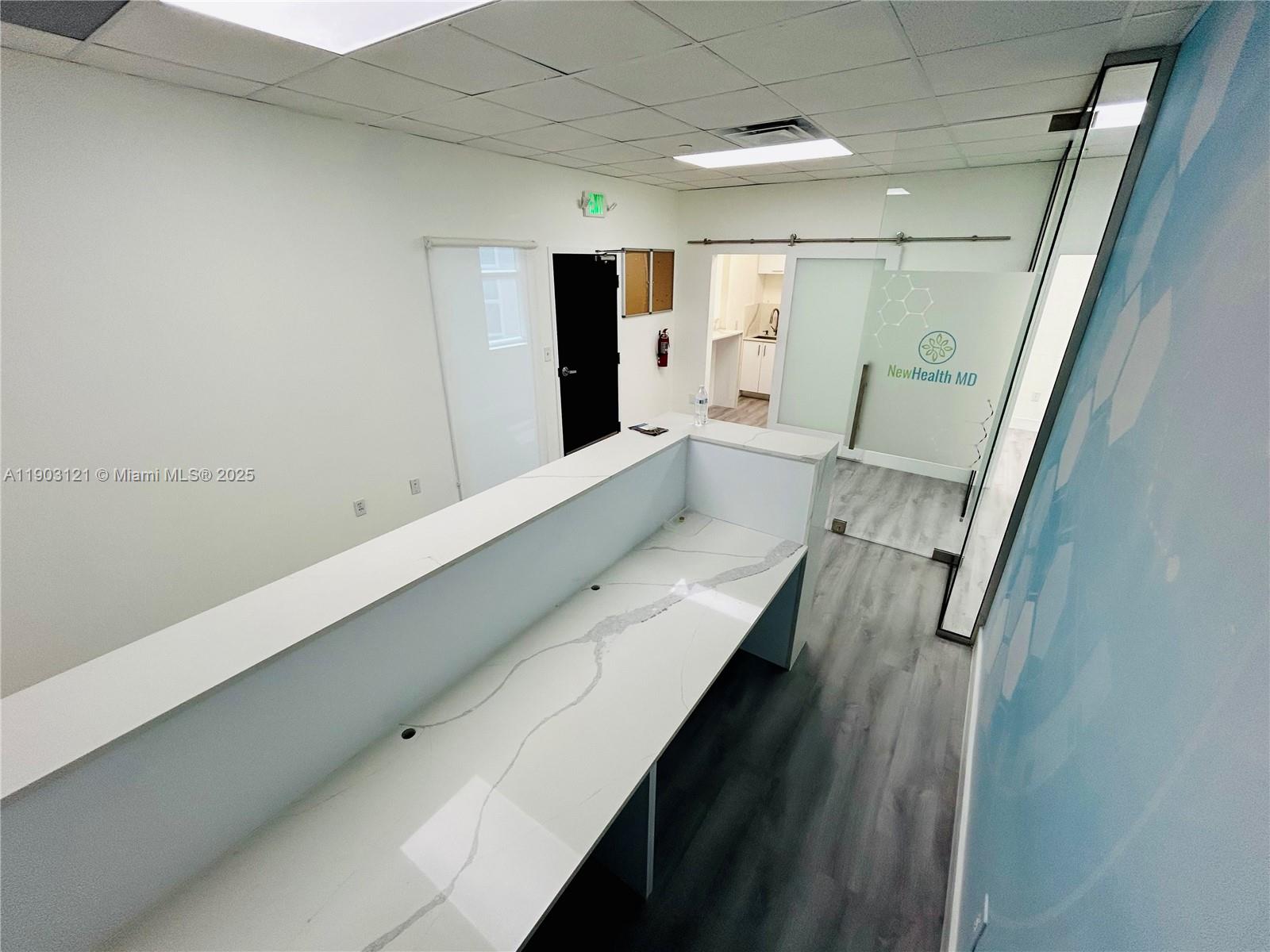 A reception area features a white marble-topped desk, gray wood-look flooring, and glass sliding doors — 10305 NW 41st St # 216, Doral FL 33178, DORAL, FL