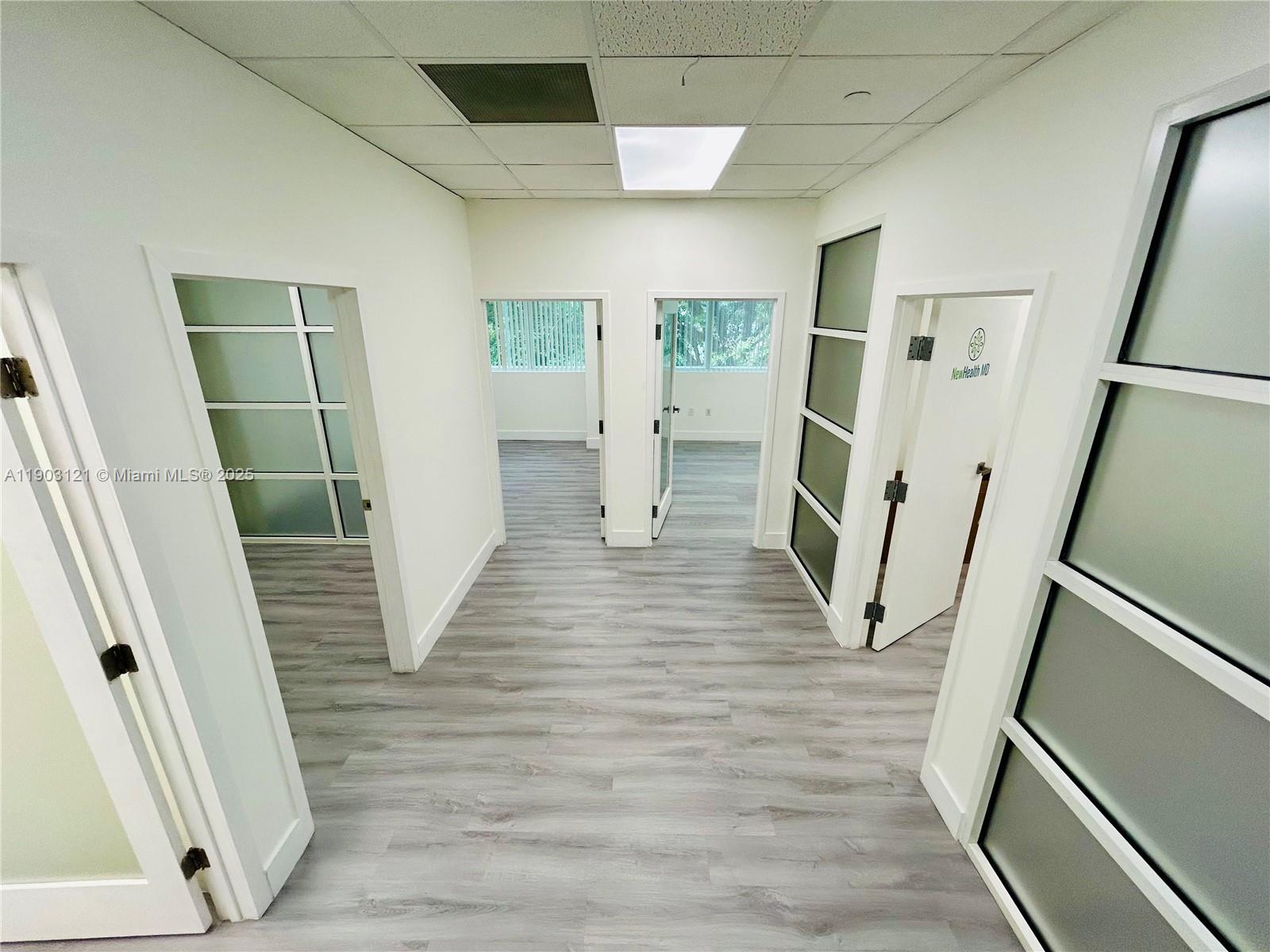 A hallway with light wood-look flooring leads to multiple office doors with glass panels — 10305 NW 41st St # 216, Doral FL 33178, DORAL, FL
