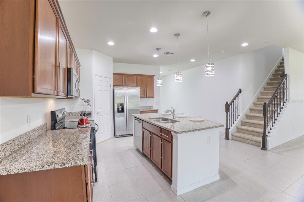 A kitchen with wood cabinets, granite countertops, a center island, and stairs to the right — 5270 BRYDON WOODS CIRCLE, ST CLOUD, FL
