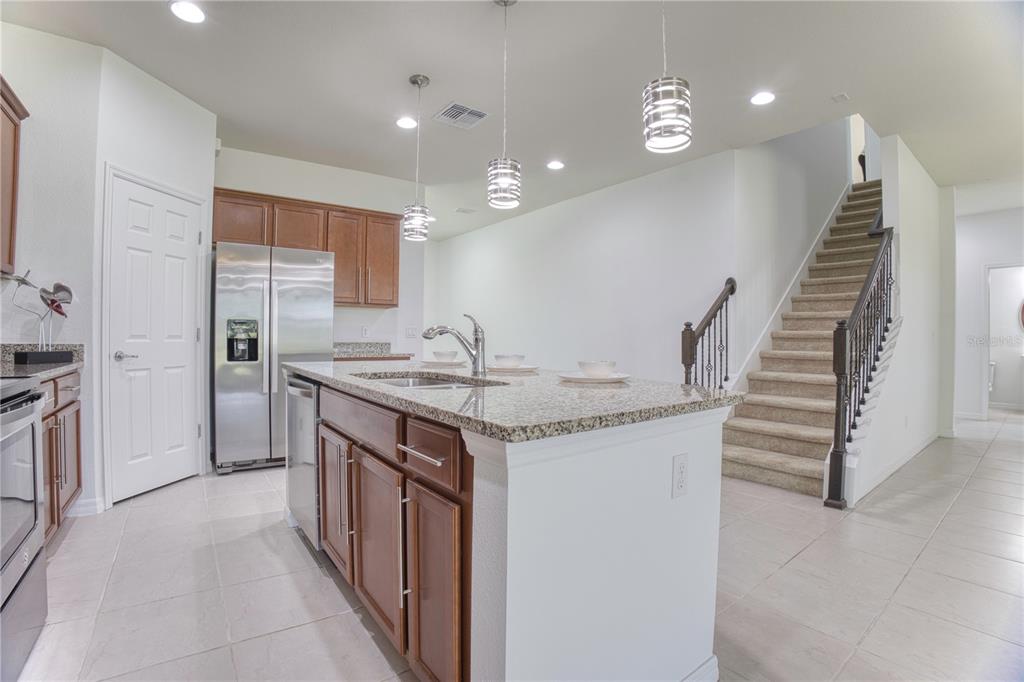 A kitchen with wood cabinets, granite countertops, a center island, and stairs leading upstairs — 5270 BRYDON WOODS CIRCLE, ST CLOUD, FL