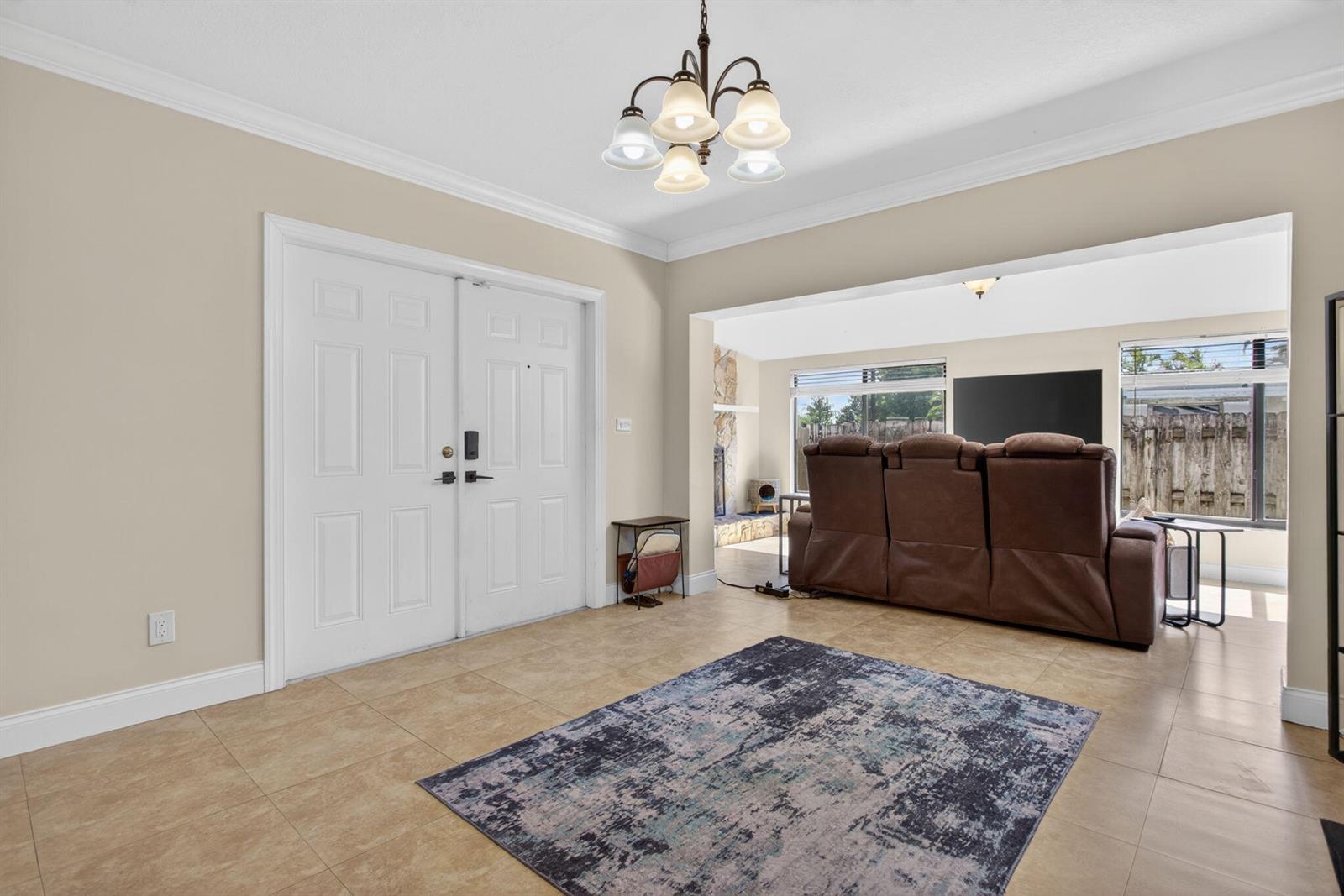 An entryway with tile flooring and a chandelier leads into a living room with furniture — 1914 NE 53rd Court, Pompano Beach FL 33064, POMPANO BEACH, FL