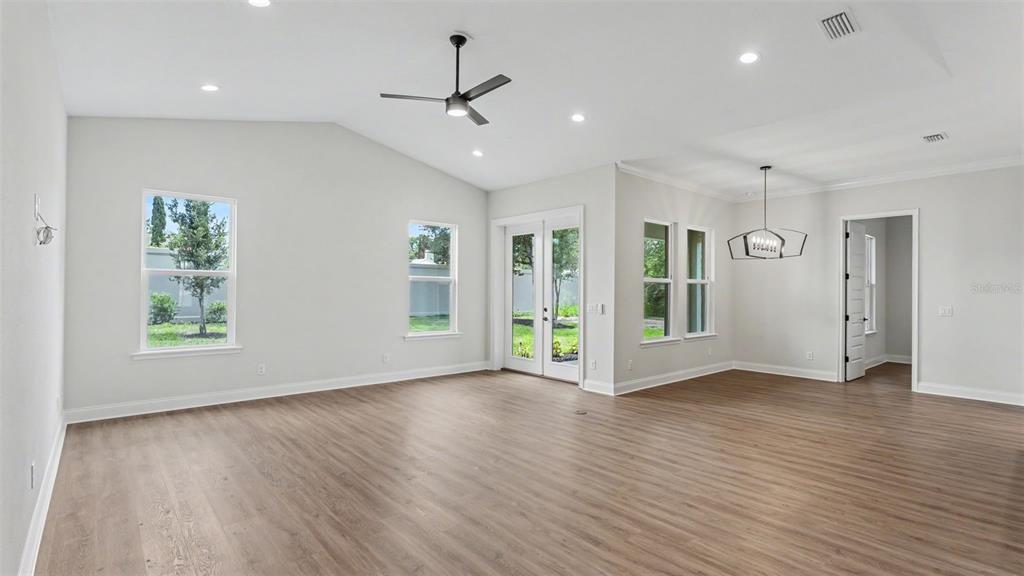 An open-concept living area features light wood-look flooring, a kitchen island, and glass patio doors — 5367 CLUBHOUSE HILLS LANE, LAKELAND, FL