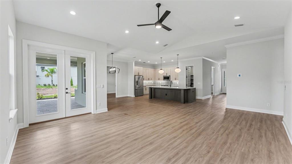 An empty living room features light gray walls, wood-look flooring, a ceiling fan, and two windows — 5367 CLUBHOUSE HILLS LANE, LAKELAND, FL