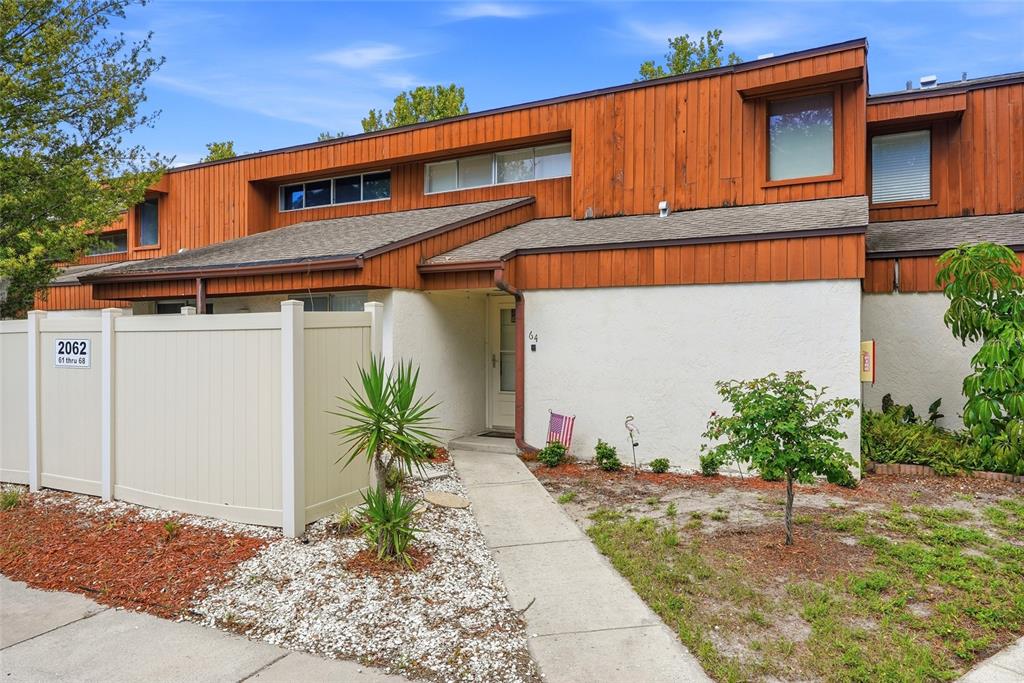 A two-story townhouse exterior features brown wood siding, white stucco walls, and a concrete walkway — 2062 SUNSET POINT ROAD UNIT 64, CLEARWATER, FL