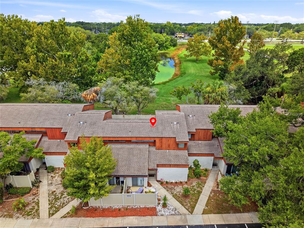 An aerial view shows a multi-unit townhouse complex with a pond and trees behind it — 2062 SUNSET POINT ROAD UNIT 64, CLEARWATER, FL