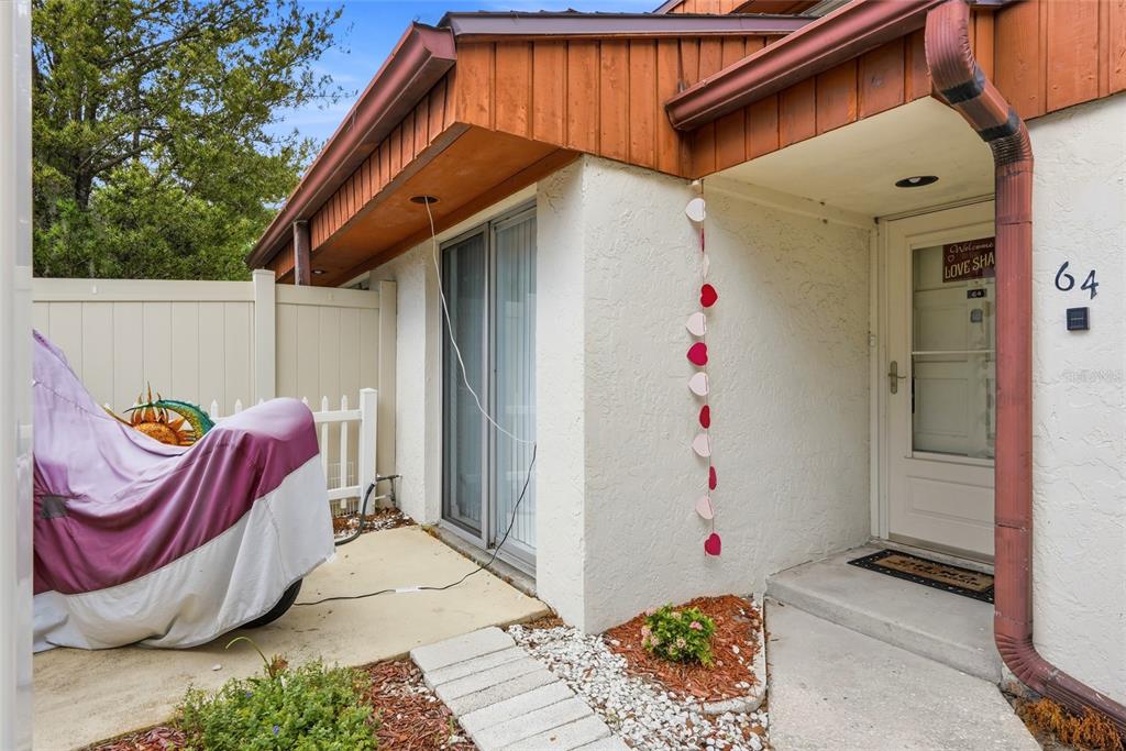 The exterior of a home features a white stucco wall, a sliding door, and a walkway — 2062 SUNSET POINT ROAD UNIT 64, CLEARWATER, FL