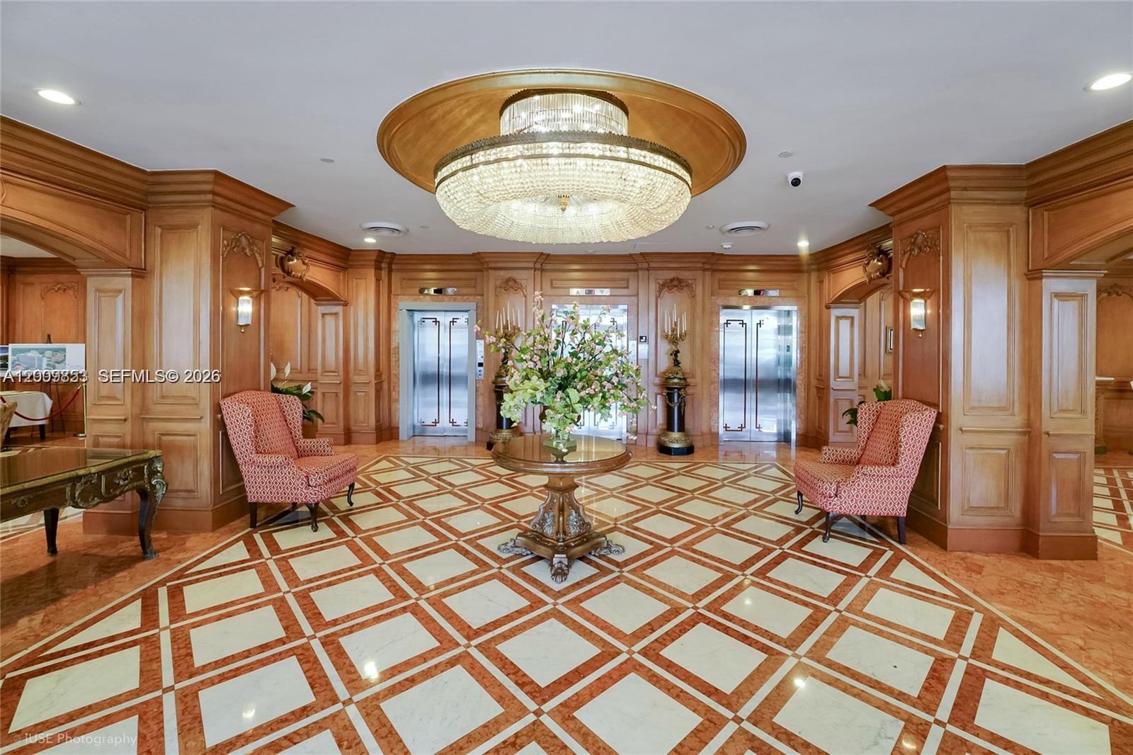 A formal elevator lobby features wood-paneled walls, a crystal chandelier, and patterned marble flooring — 700 Biltmore Way # 504, Coral Gables FL 33134, CORAL GABLES, FL