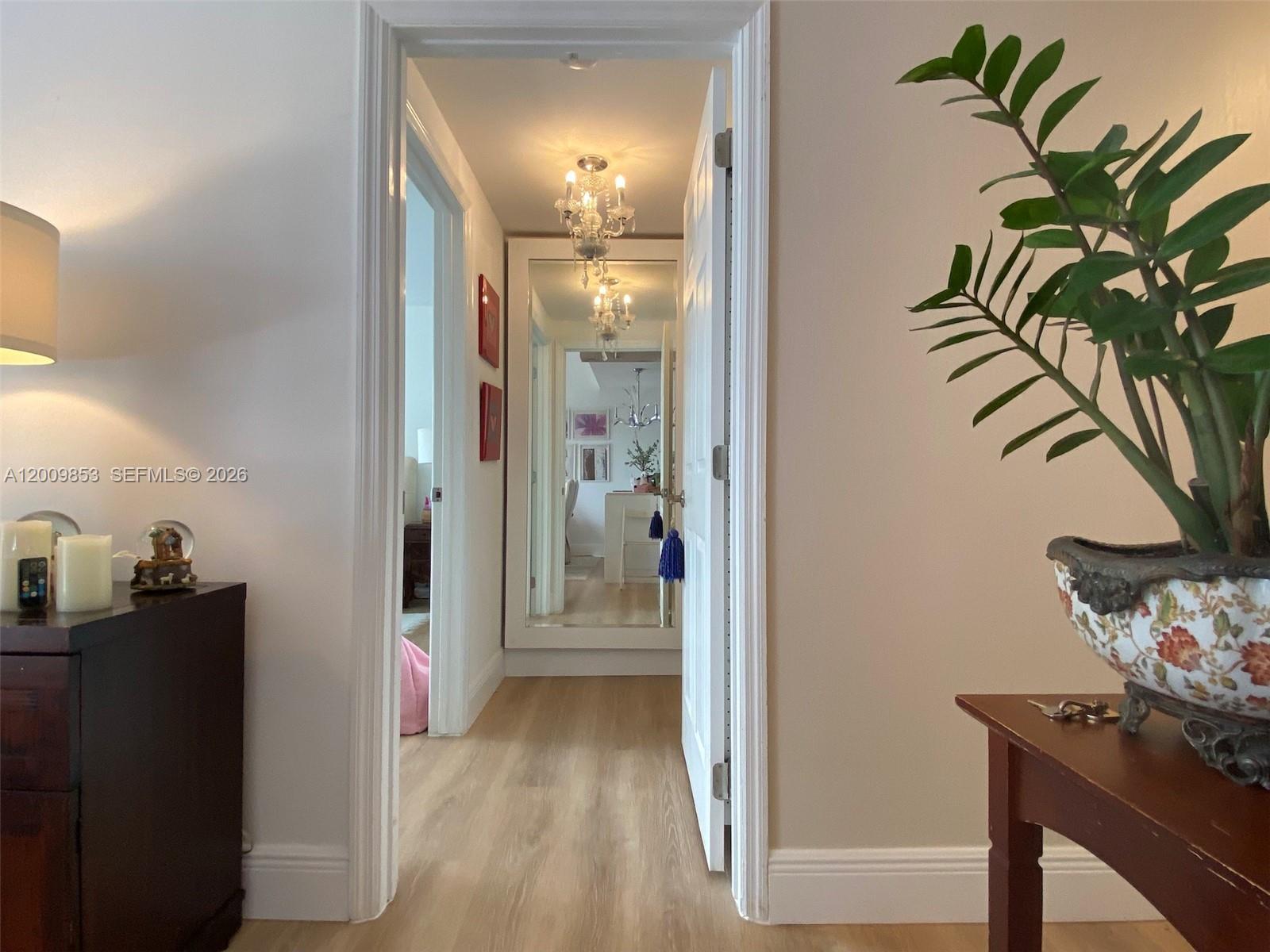 A hallway with light wood flooring leads to a large mirror and a crystal chandelier — 700 Biltmore Way # 504, Coral Gables FL 33134, CORAL GABLES, FL