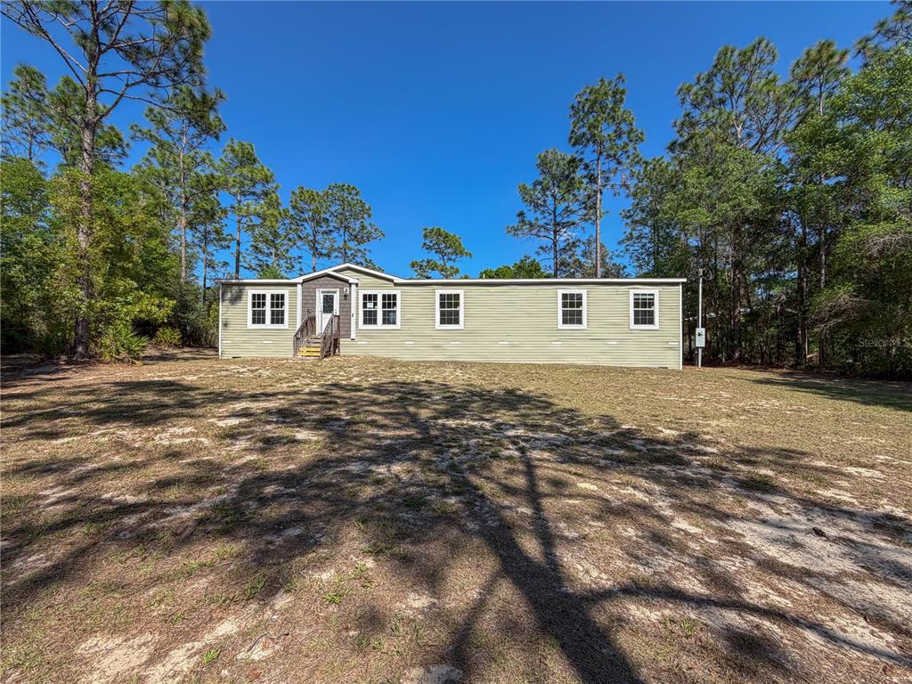 A single-story manufactured home with light green siding sits on a sandy, wooded lot — 4497 NE 142ND AVENUE, WILLISTON, FL