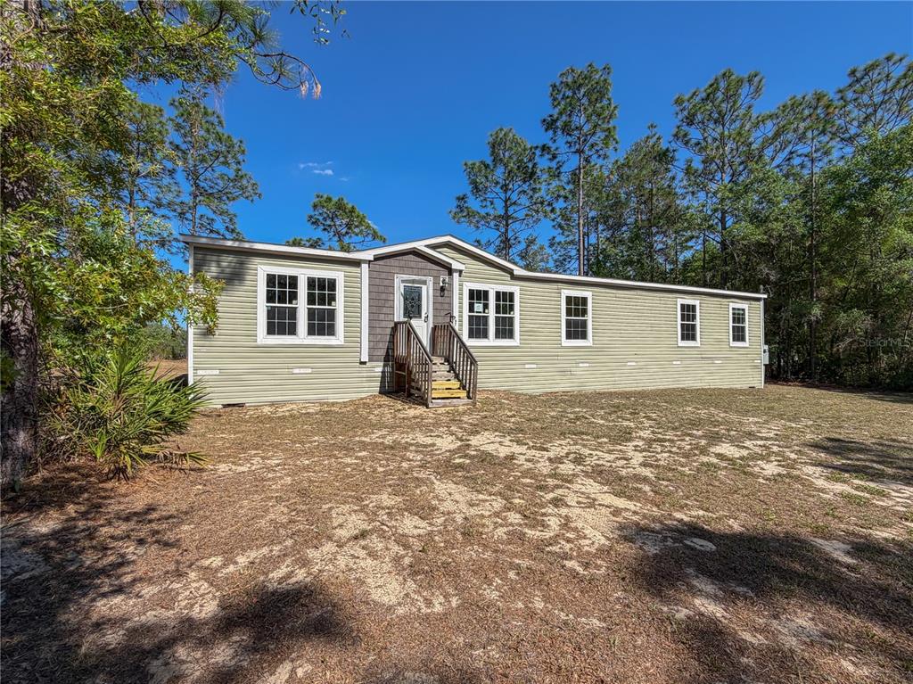 A single-story manufactured home with light green siding sits on a sandy, wooded lot — 4497 NE 142ND AVENUE, WILLISTON, FL