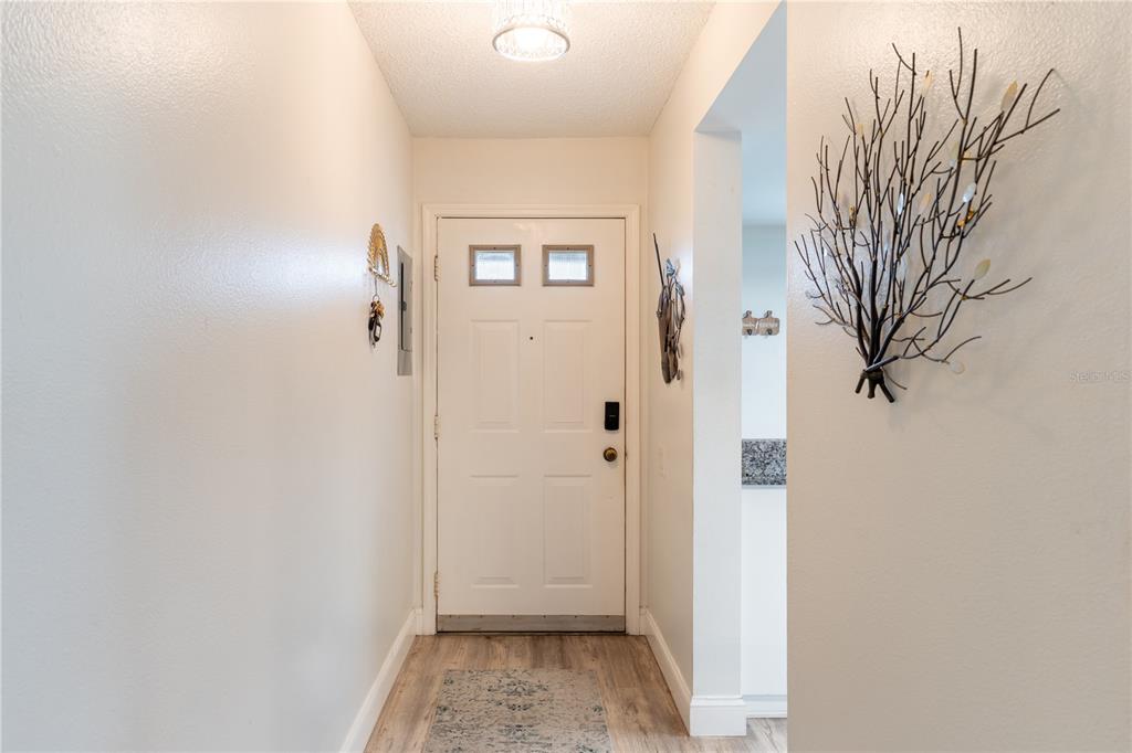 An entryway features a white front door, light wood-look flooring, and decorative wall art — 2170 ELM STREET UNIT 901, DUNEDIN, FL