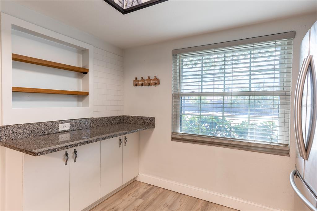 A kitchen area features white cabinets, granite countertops, open wood shelving, and a window with blinds — 2170 ELM STREET UNIT 901, DUNEDIN, FL