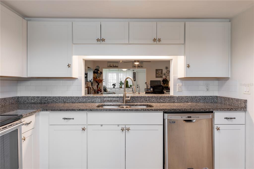 A kitchen features white cabinets with star-shaped knobs, granite countertops, and a pass-through window — 2170 ELM STREET UNIT 901, DUNEDIN, FL