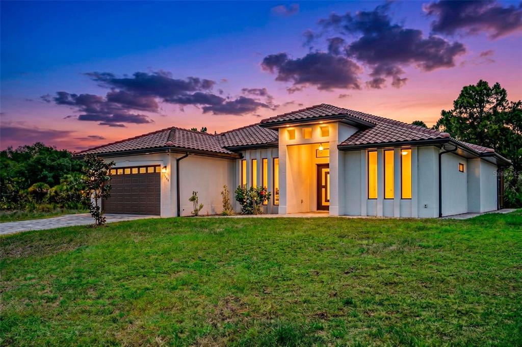 A single-story house with a tile roof, garage, and illuminated windows at sunset — 12347 DURANGO AVENUE, NORTH PORT, FL