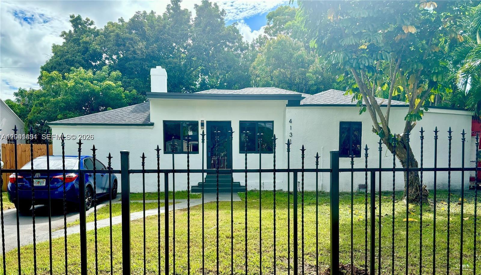A white single-story house with a dark roof and black trim sits behind a metal fence — 4131 NW 11th Pl, Miami FL 33127, MIAMI, FL