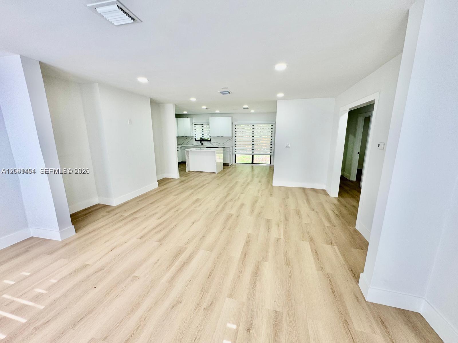 An open-concept living area features light wood-look flooring, white walls, and a modern kitchen — 4131 NW 11th Pl, Miami FL 33127, MIAMI, FL