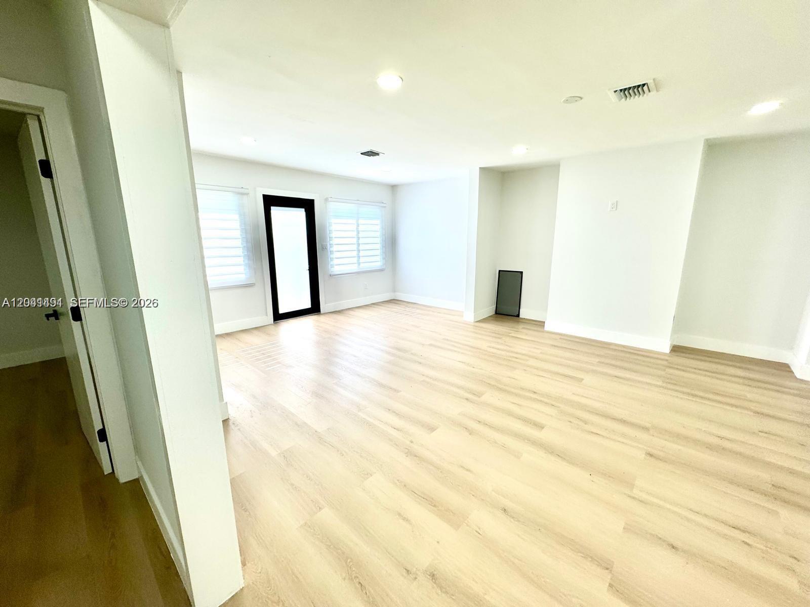 A bright, empty room features light wood-look flooring, white walls, and a glass-paned door — 4131 NW 11th Pl, Miami FL 33127, MIAMI, FL