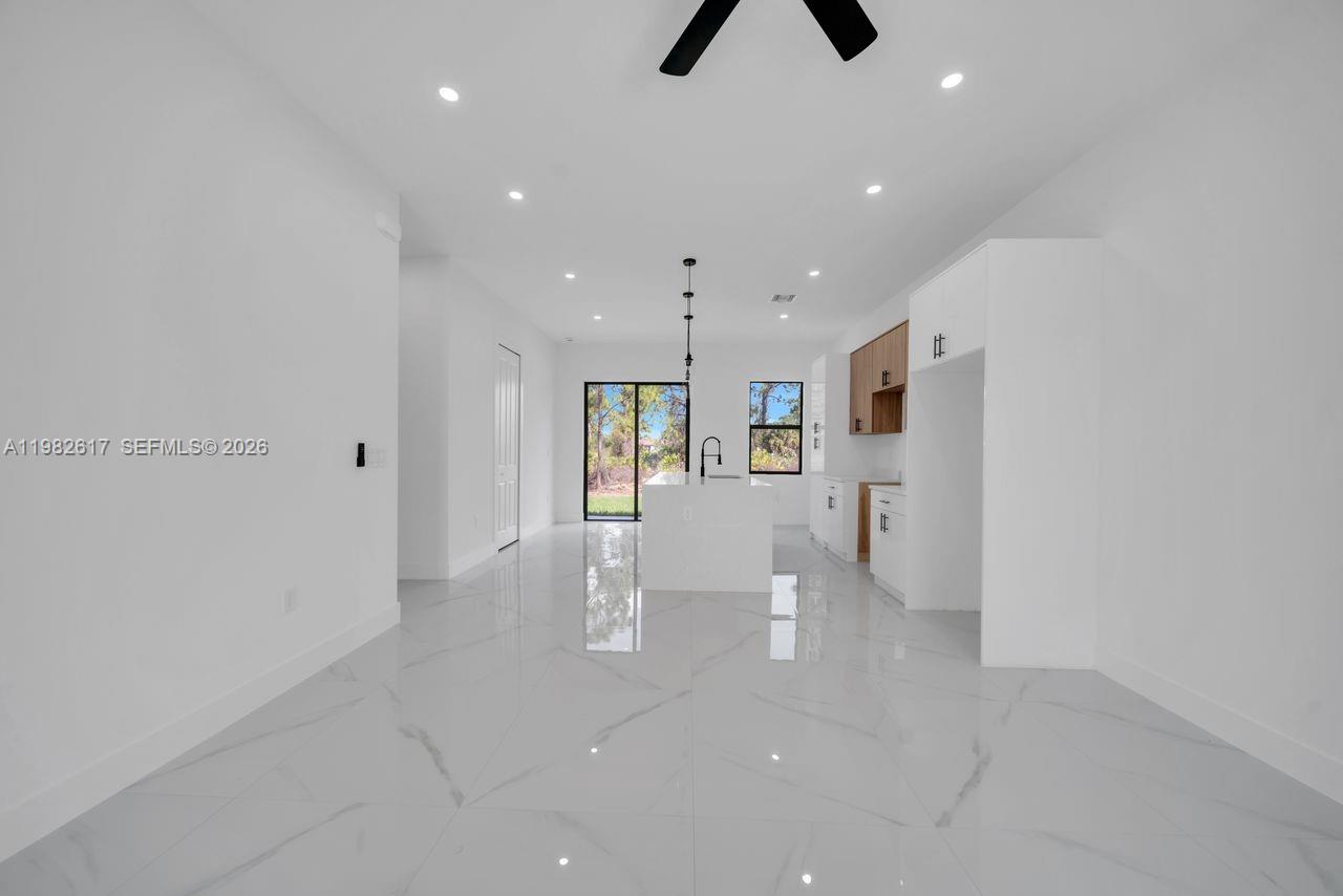 A modern, open-concept kitchen and living area features white cabinetry, marble-look tile flooring, and recessed lighting — 637 Summit Ave S, Lehigh Acres FL 33974, LEHIGH ACRES, FL