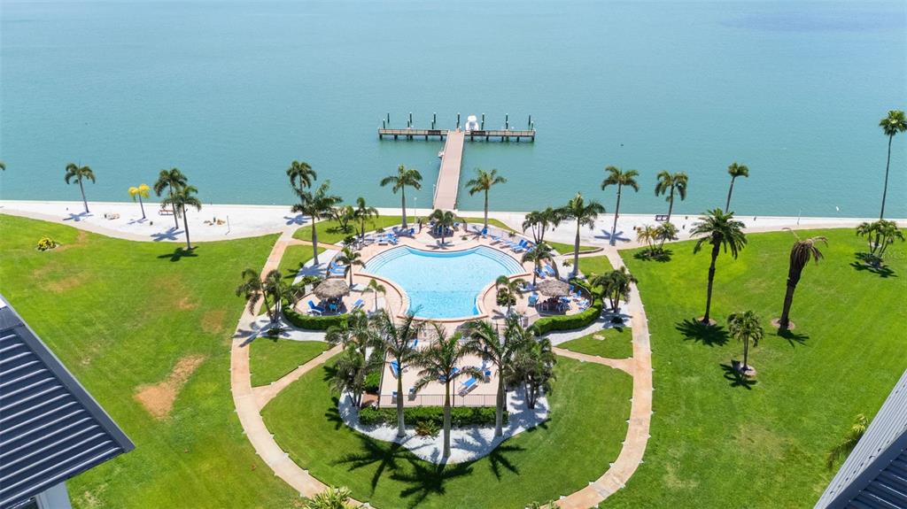 An aerial view shows a swimming pool, palm trees, and a pier on the water — 5130 BRITTANY DRIVE S UNIT 505, ST PETERSBURG, FL
