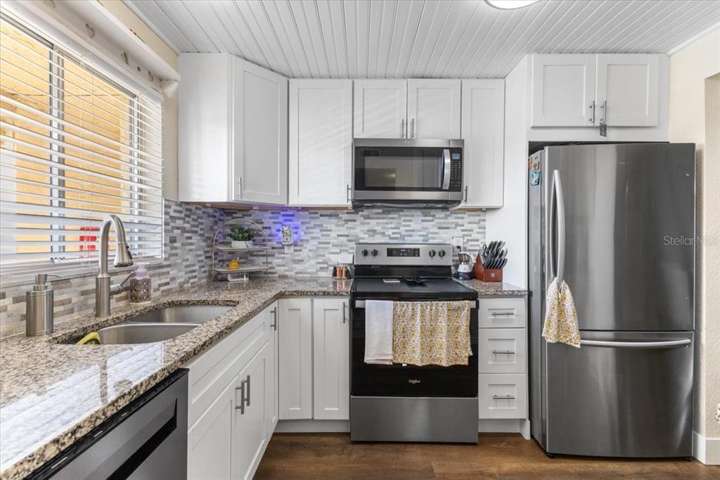 A kitchen features white cabinets, granite countertops, a stainless steel refrigerator, and a tile backsplash — 3710 LAKE BAYSHORE DRIVE UNIT k416, BRADENTON, FL