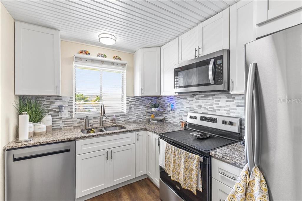 A kitchen features white cabinets, stainless steel appliances, granite countertops, and a tiled backsplash — 3710 LAKE BAYSHORE DRIVE UNIT k416, BRADENTON, FL