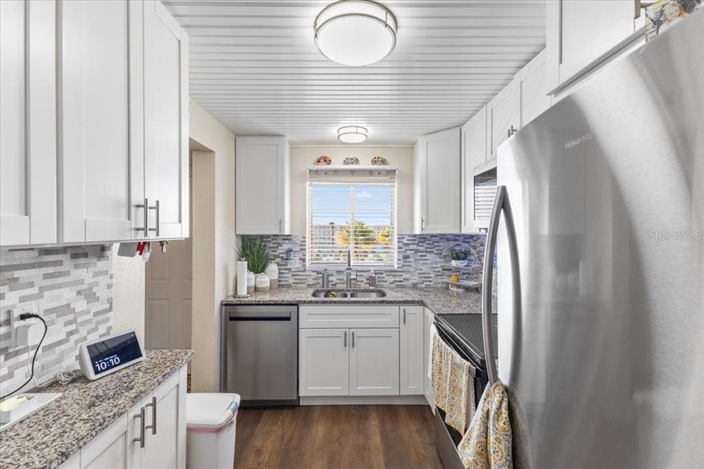 A kitchen features white cabinets, stainless steel appliances, granite countertops, and a tiled backsplash — 3710 LAKE BAYSHORE DRIVE UNIT k416, BRADENTON, FL
