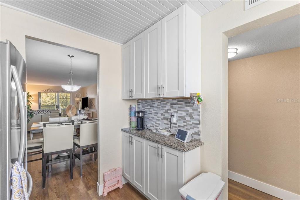 A kitchen coffee station features white cabinets, granite countertops, and a gray tiled backsplash — 3710 LAKE BAYSHORE DRIVE UNIT k416, BRADENTON, FL