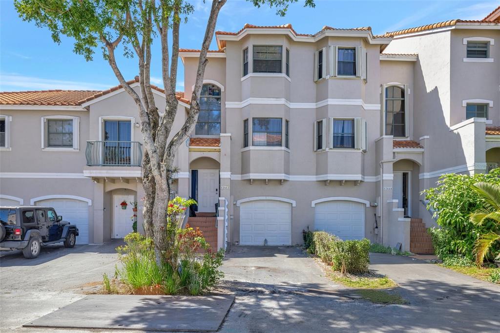 A multi-story townhouse exterior features beige stucco walls, multiple garage doors, and a large tree — 12662 NW 14TH STREET, SUNRISE, FL